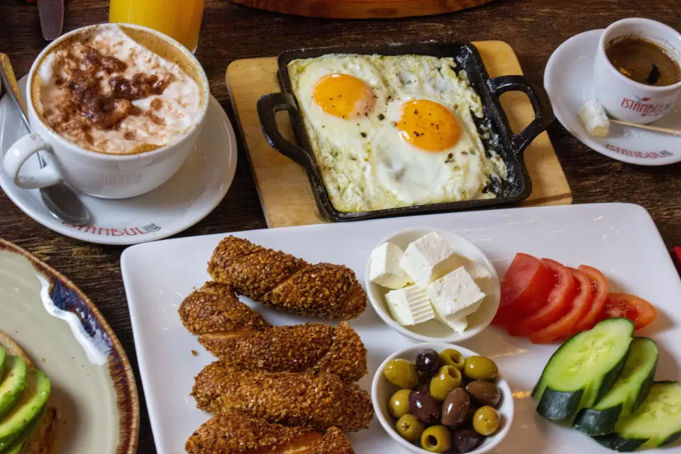 A brunch table with eggs, sucuk, simit, coffee and orange juice