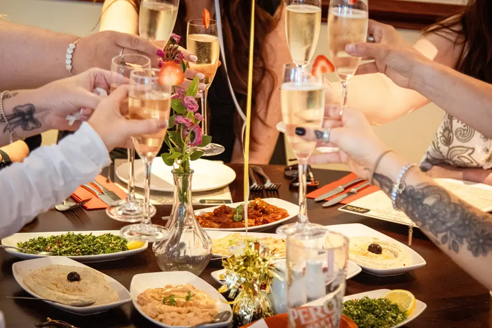 Friends raising glasses of prosecco over a table of meze