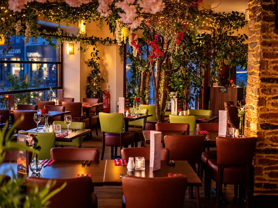 The dining room under cherry blossom and hanging greenery, with a sandstone wall and red leather chairs