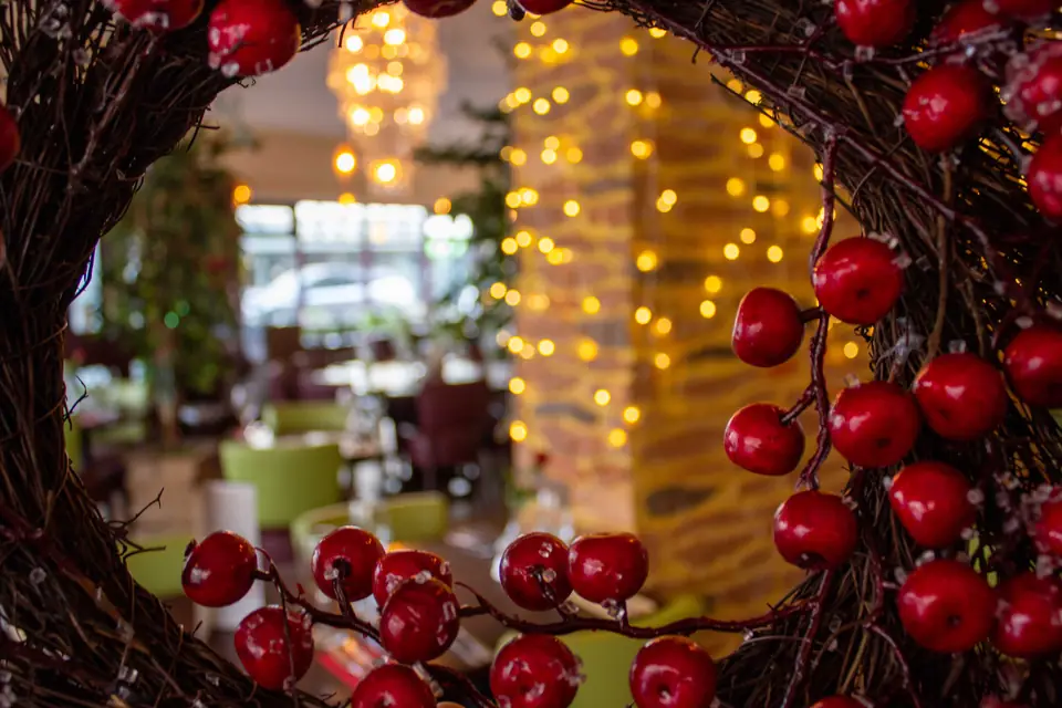 The dining room seen through a Christmas wreath of red berries, with fairy lights on the sandstone wall